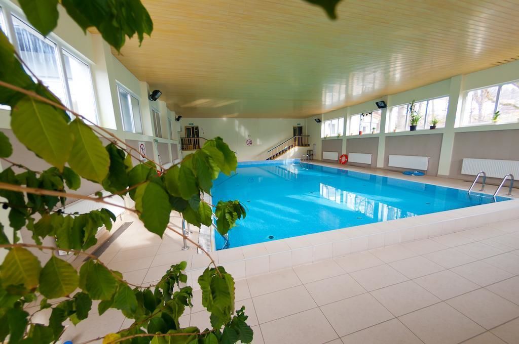 Ein Innenpool mit klarem, blauem Wasser, umgeben von weiß gefliesten Böden und Wänden sowie großen Fenstern, die natürliches Licht hereinlassen.