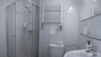 A modern bathroom with a glass-enclosed shower, a toilet with a paper towel holder, and a sink with a soap dispenser.