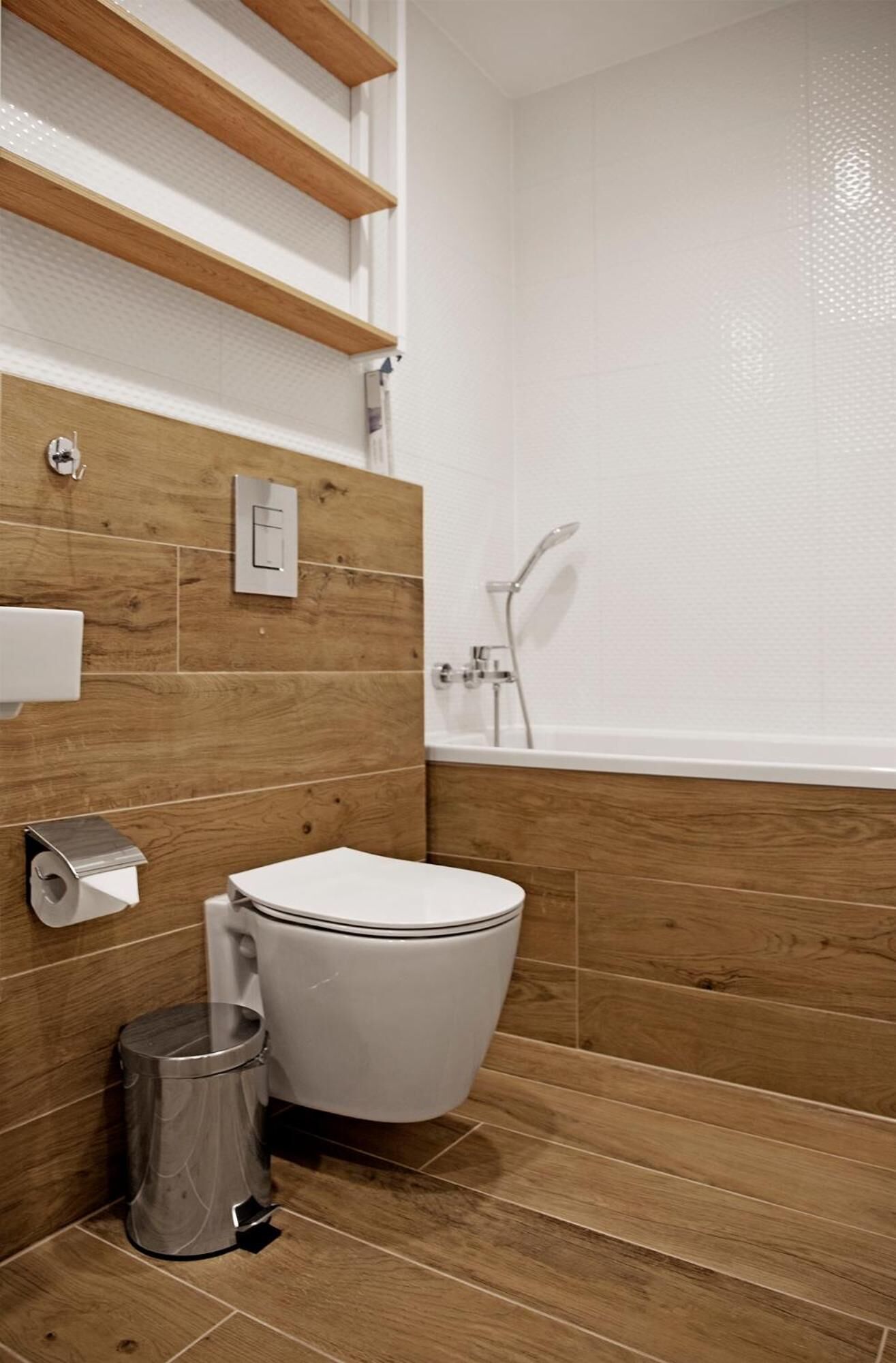 Un baño moderno con tocador de madera, inodoro, cubo de basura y bañera.