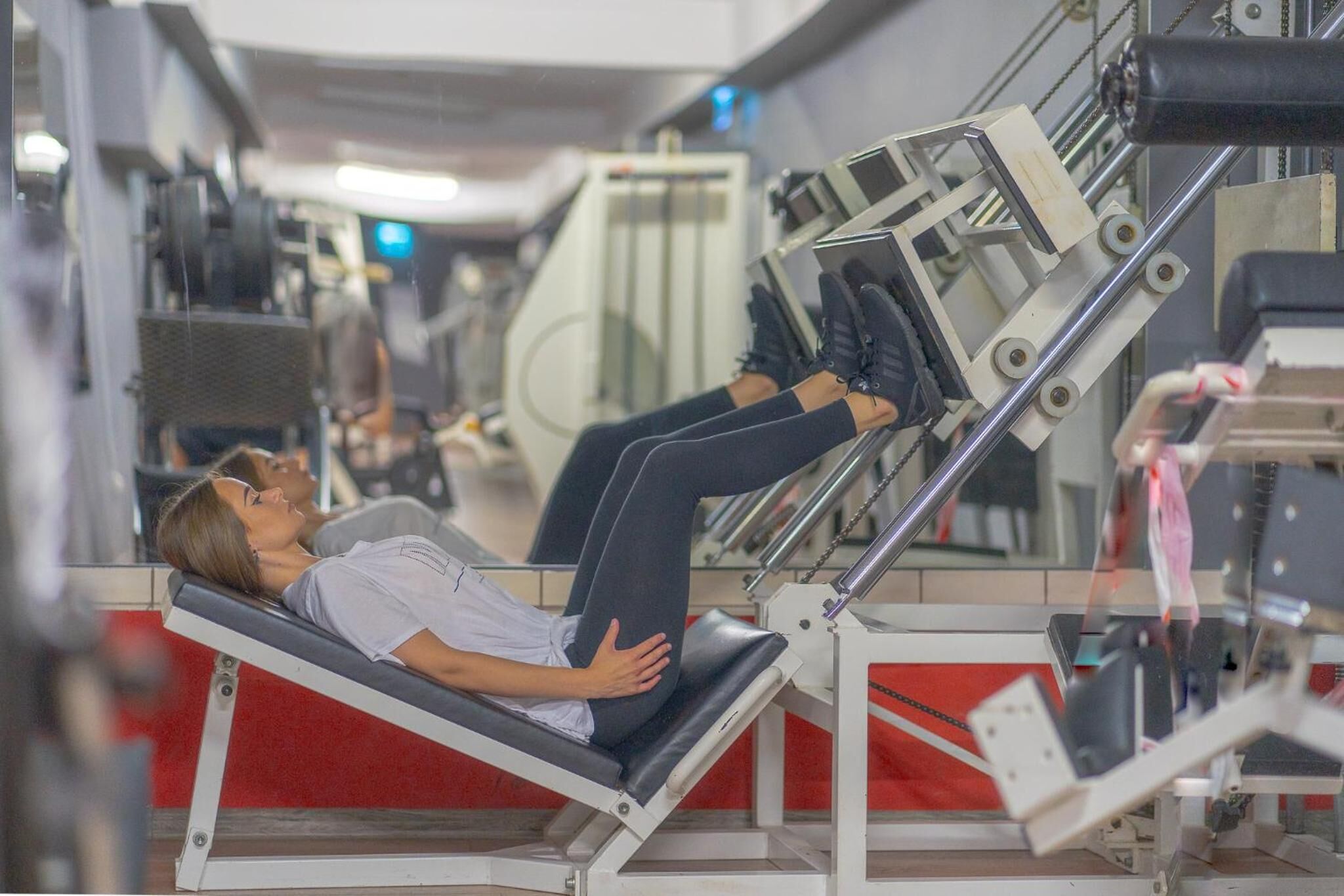 A person lying on a gym equipment with a mirror and red flooring.
