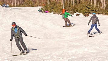 A snowy ski slope with skiers and a forest in the background.