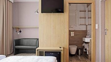 Una habitación de hotel con cama, escritorio con televisor, silla y baño con lavamanos e inodoro.