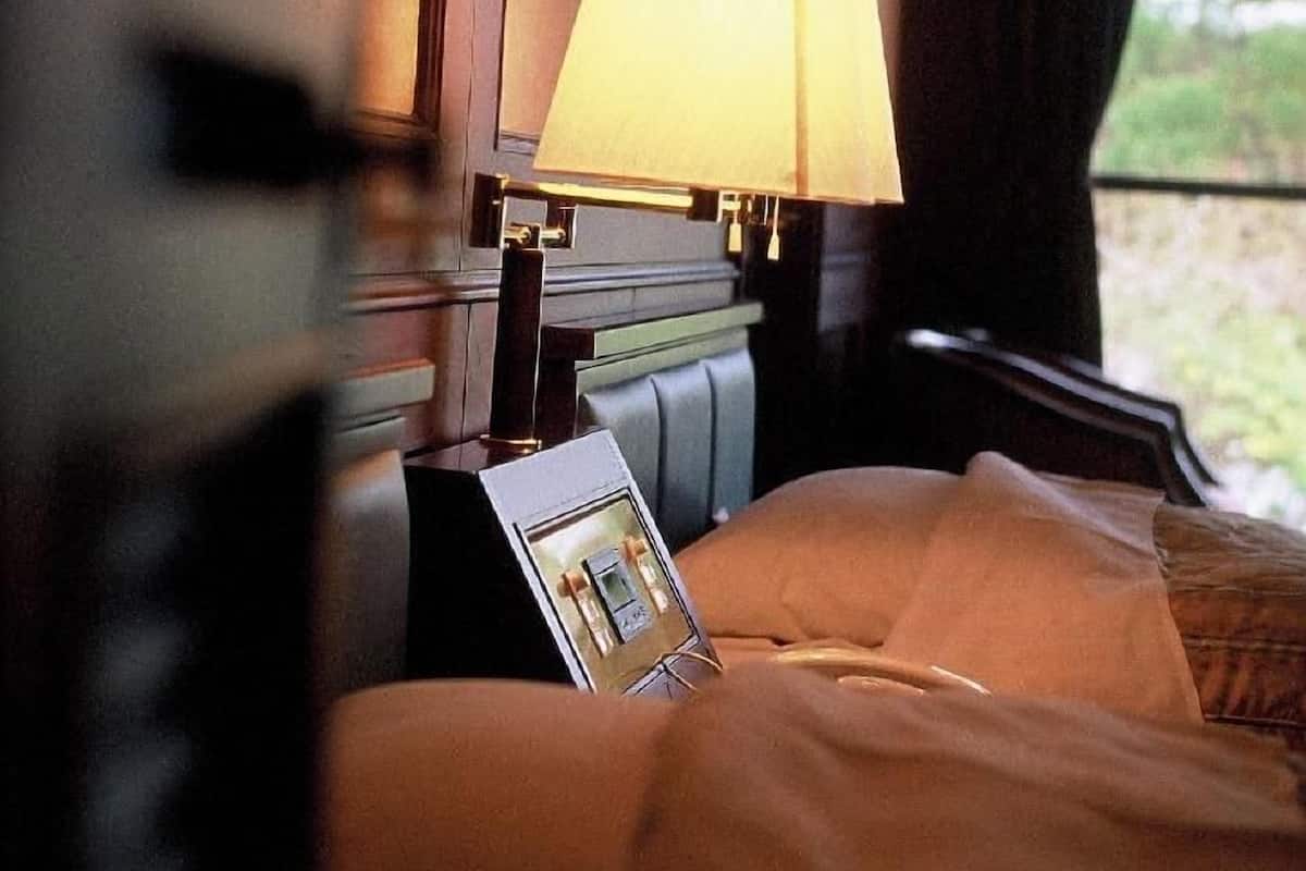 Quarto de hotel com cama, mesa de cabeceira, luminária e janela com vista.