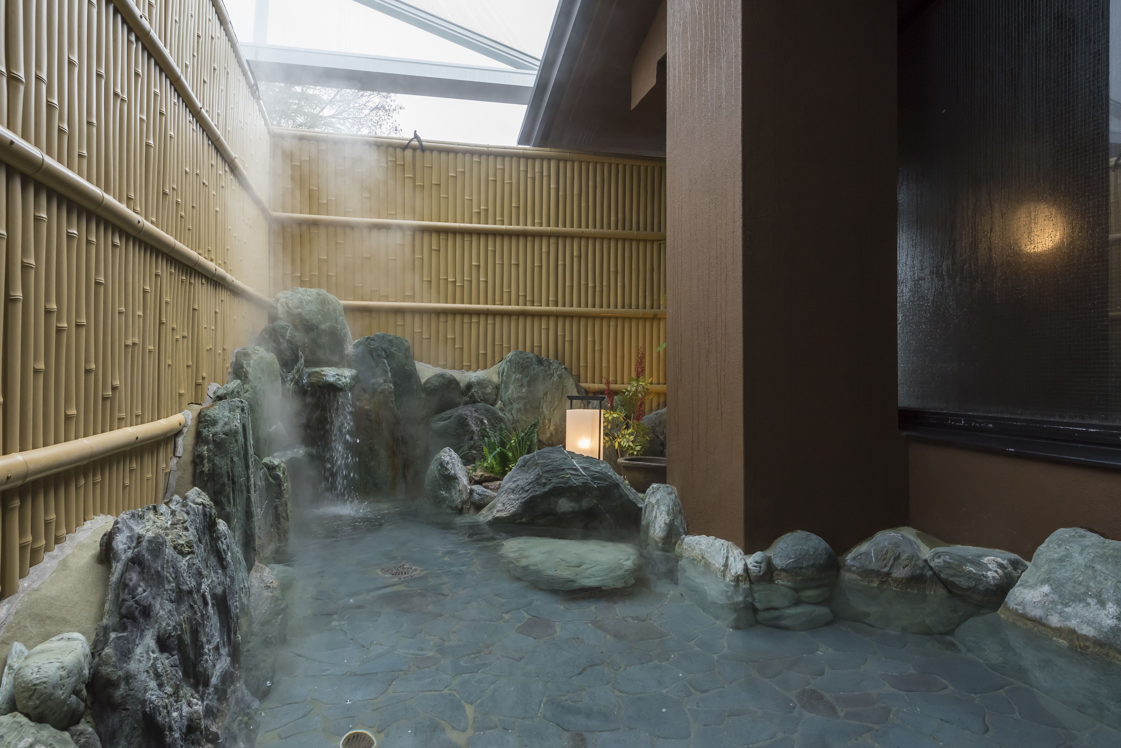 Un jardín japonés tradicional con una fuente de agua de piedra, paredes de bambú y un farol.