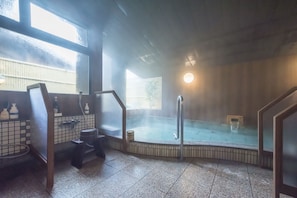 A traditional Japanese onsen with a wooden interior, a hot spring bath, and a view of the outside.