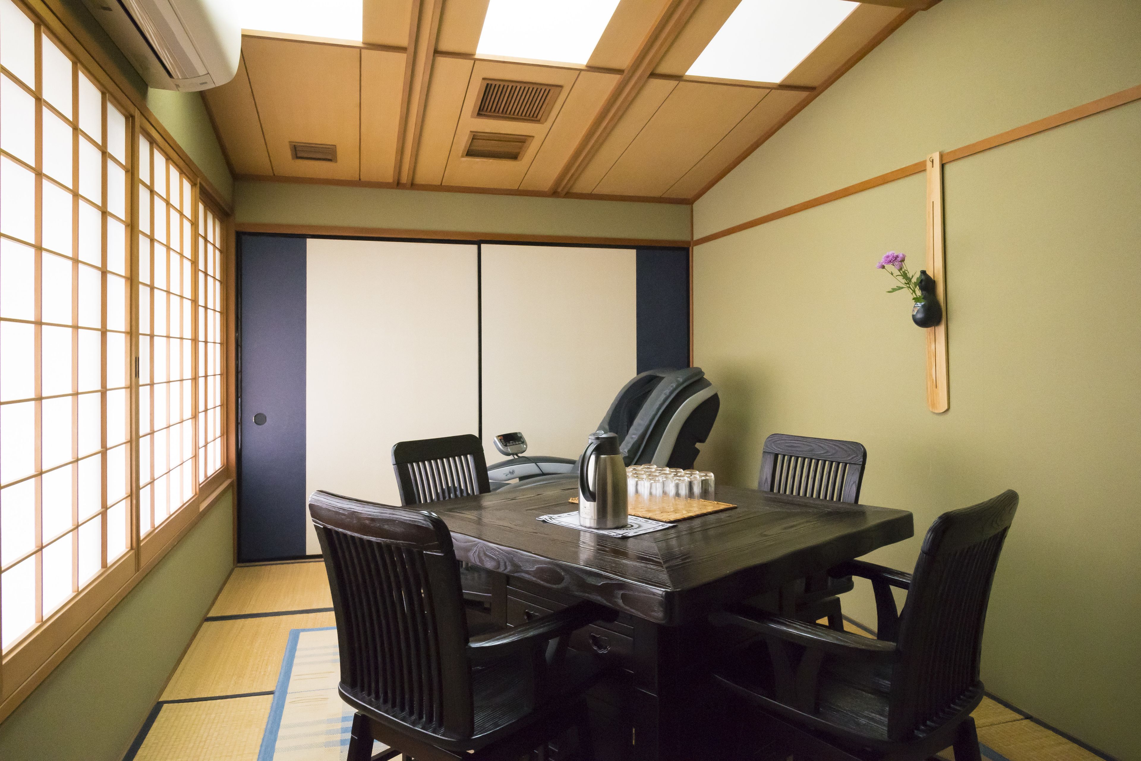 A traditional Japanese-style meeting room with tatami flooring, a dark wooden table, black chairs, and a shoji screen door.