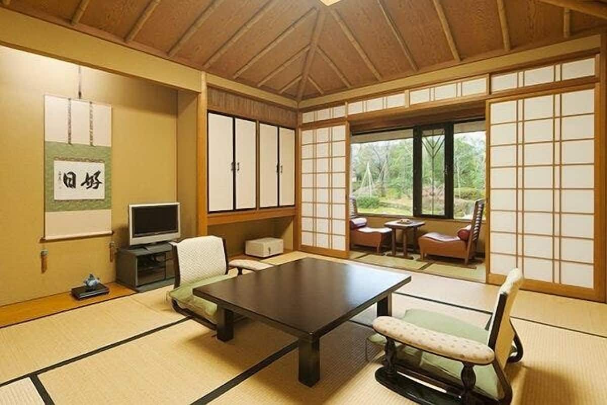 Une pièce de style japonais traditionnel, avec un sol recouvert de tatamis, une table basse, un téléviseur et des portes coulissantes donnant sur un jardin.