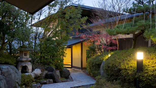 Ein traditionelles japanisches Haus mit einem Kiesweg, der zum Eingang führt, umgeben von Steinen und Grünpflanzen.