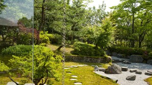 Ein traditioneller japanischer Garten mit Pflastersteinen, einer Steinmauer und verschiedenen Bäumen.