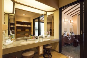 A hotel bathroom with a large mirror, two sinks, and a vanity area.