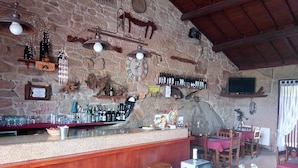 Un rústico bar con taburetes de madera, pared de piedra y varias botellas y adornos.