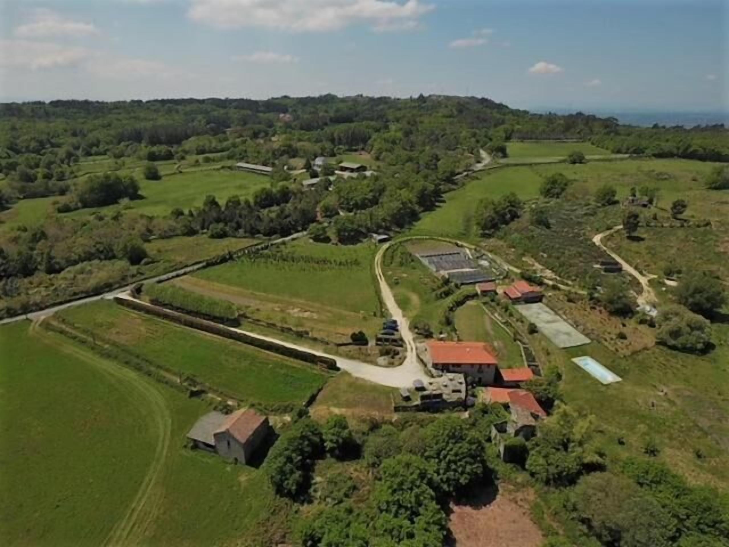 Vista aèria d'una finca rural amb camps, un camí sinuós i diversos edificis amb teulades vermelles.