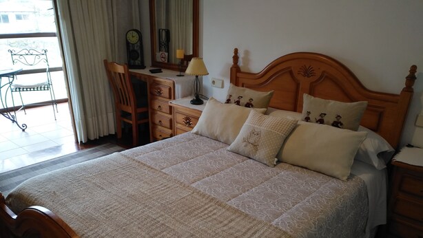 Un dormitorio con una cama grande, cabecera de madera, un escritorio con silla, una lámpara y una ventana con cortinas.