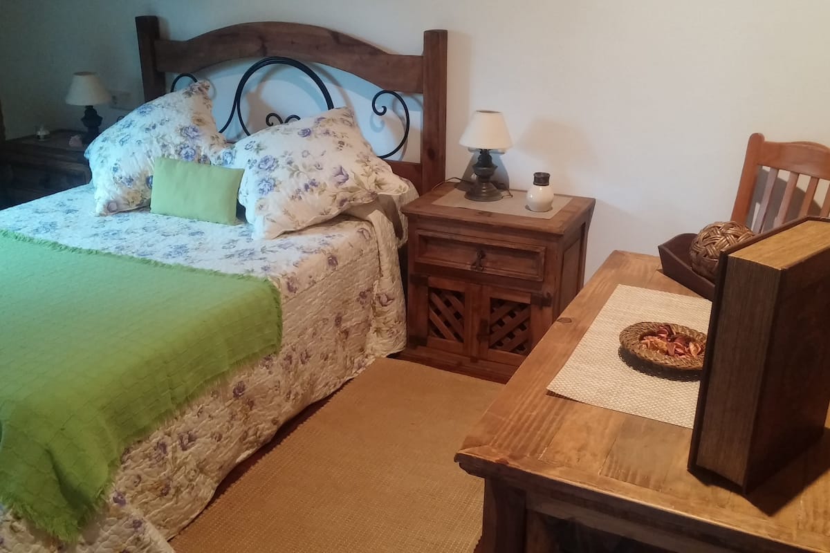 Quarto aconchegante com cama, mesa de cabeceira, mesa e cadeira.