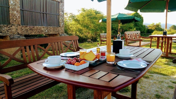 Un espacio de comedor al aire libre con bancos y mesas de madera, un frutero, platos, vasos y una botella de jugo.