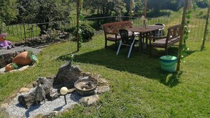 Un área de comedor al aire libre con una mesa y sillas bajo un toldo, rodeada por una cerca y follaje.