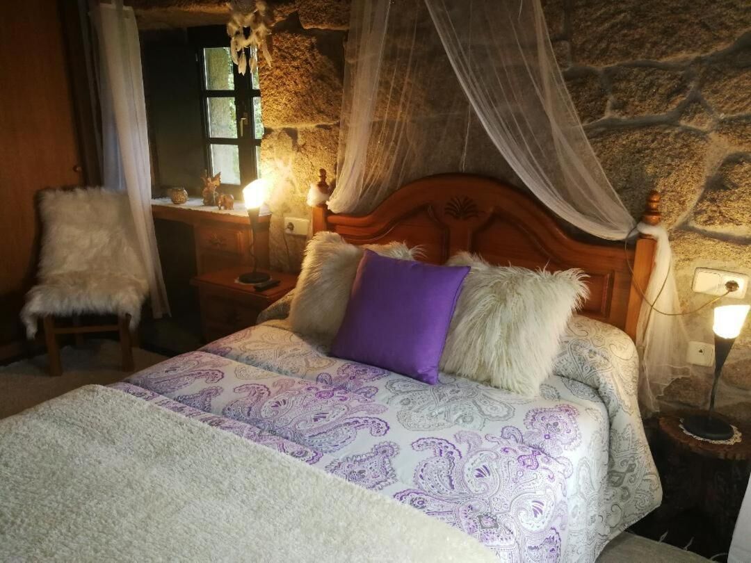 Un dormitorio con pared de piedra, una cama con dosel, un cabecero de madera y una mesita de noche con lámpara.