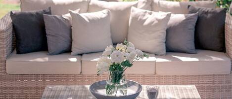 A wicker sofa with cushions and a glass coffee table with a vase of flowers.