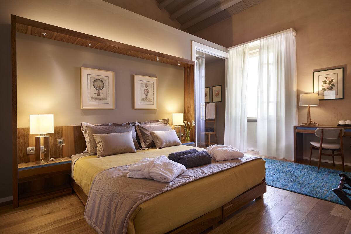 A spacious bedroom with a large bed, bedside tables, a desk, and chairs.