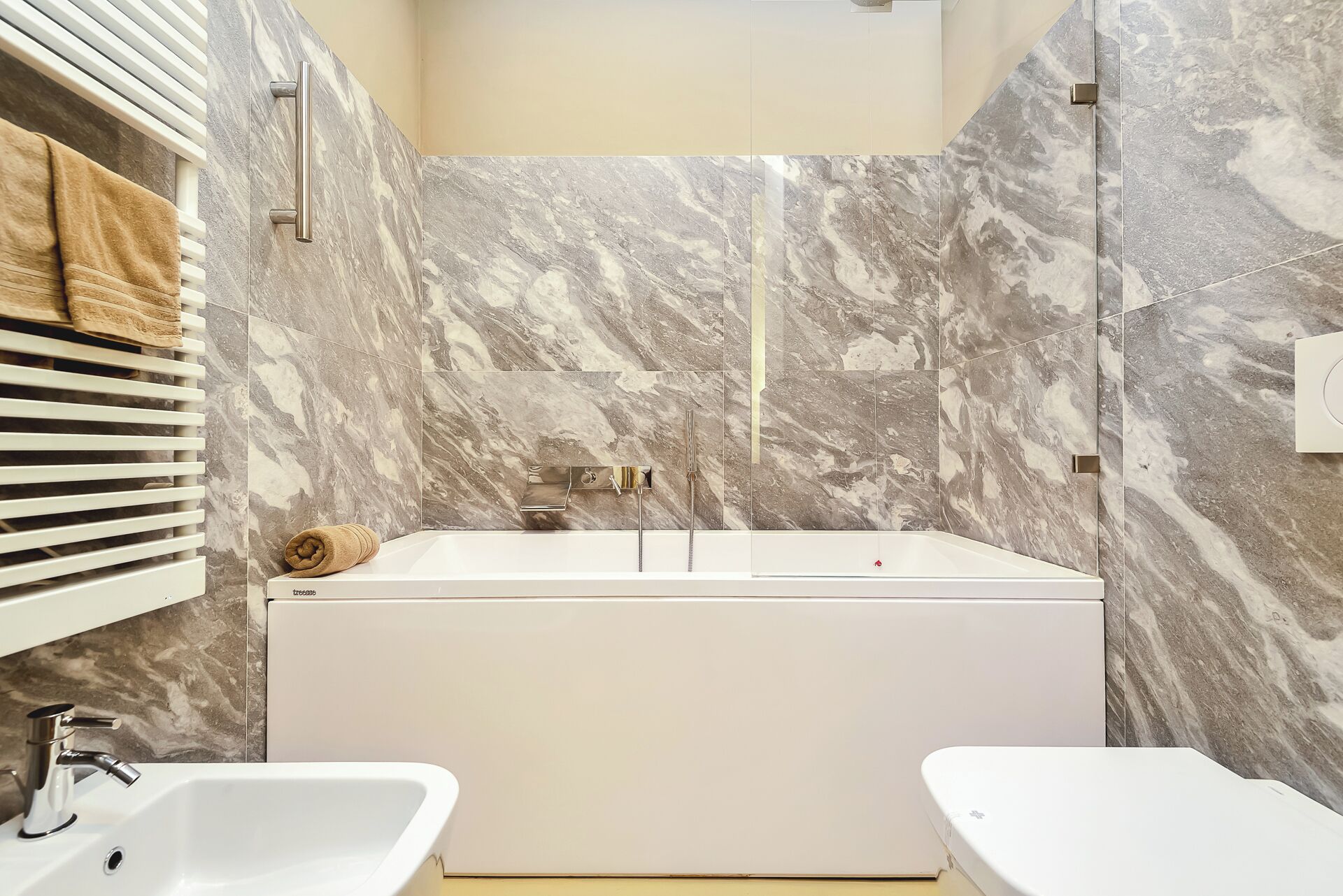 A modern bathroom with a bathtub, two sinks, and marble walls.