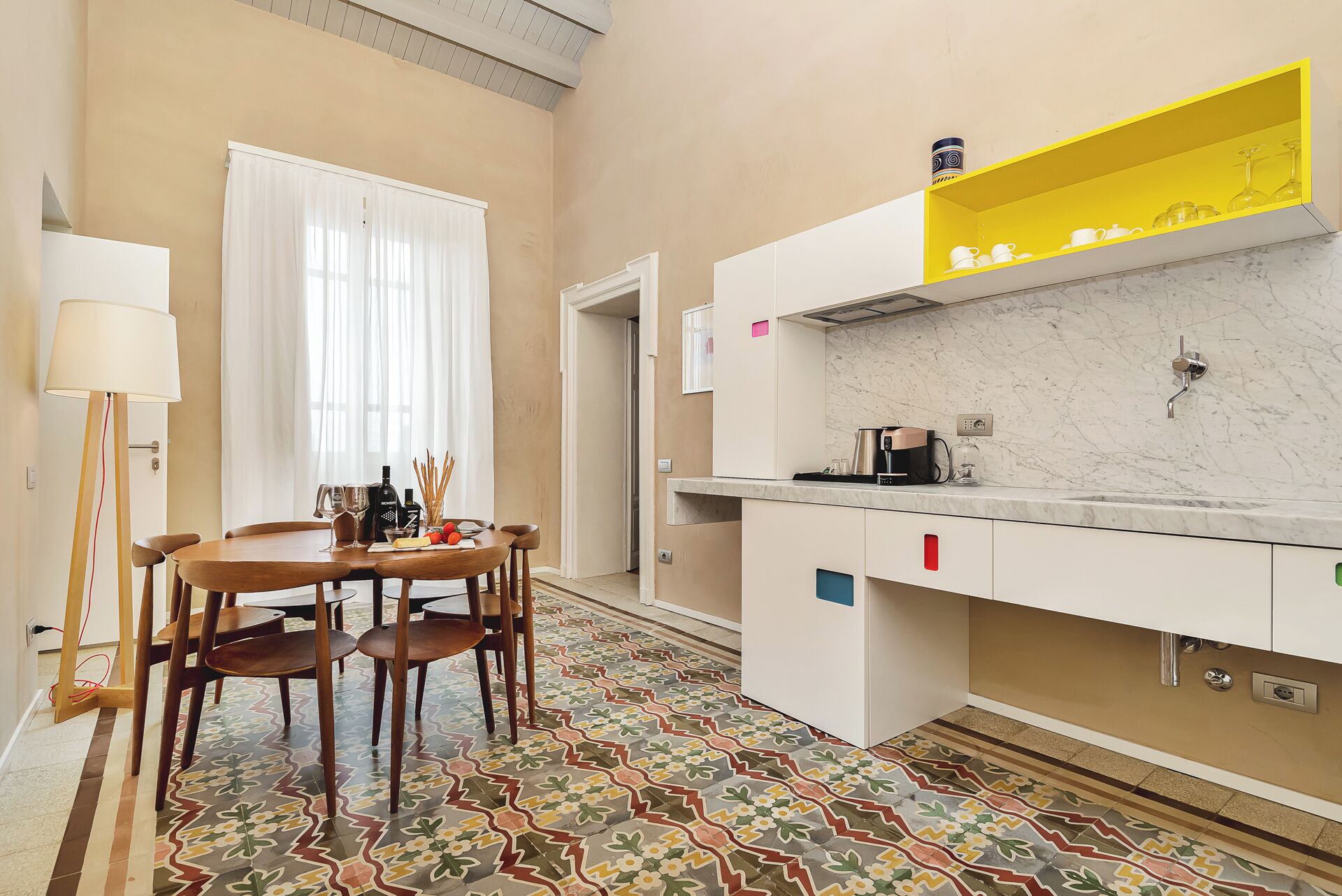 A modern kitchen with a marble countertop, a yellow shelf, and a dining area with a patterned floor.