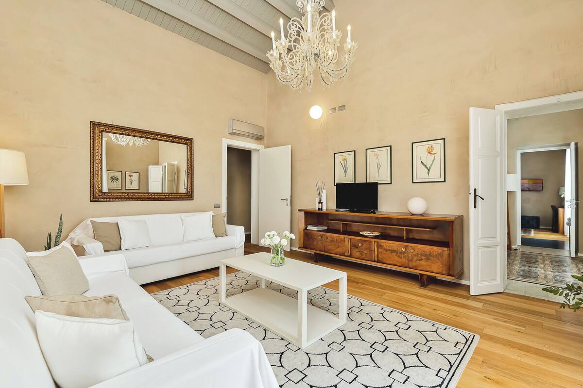 A living room with a white sofa, a coffee table, a wooden TV stand, and a chandelier.