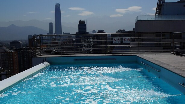 Una piscina en la azotea con vistas a un paisaje urbano, incluyendo un edificio alto al fondo.