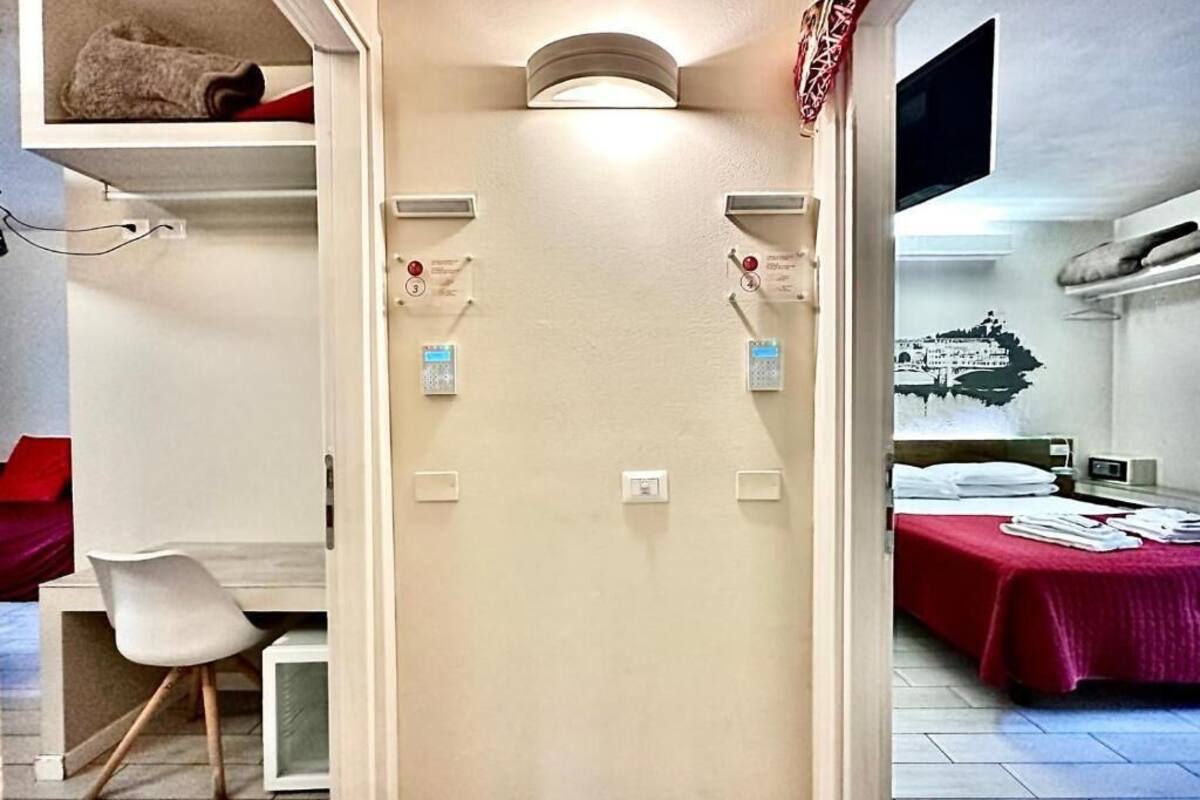 A hotel room with a bed, a desk, and a chair. There are wall-mounted controls and a flat-screen TV.
