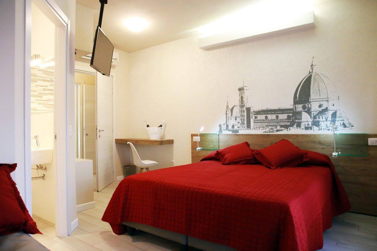 A hotel room with a bed, a desk, a chair, and a wall-mounted TV.