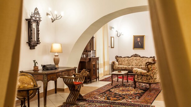 Una habitación con un escritorio de madera clásico, un globo terráqueo, una máquina de escribir antigua, un sofá estampado y una alfombra grande y ornamentada.