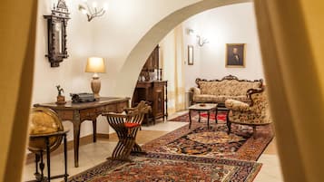 Classic design features a wooden desk, comfortable sofa, and ornate rug, complemented by an arched doorway and chandelier.