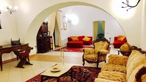 Una sala de estar con un amplio arco, un escritorio de madera, un sofá rojo y sillones estampados.