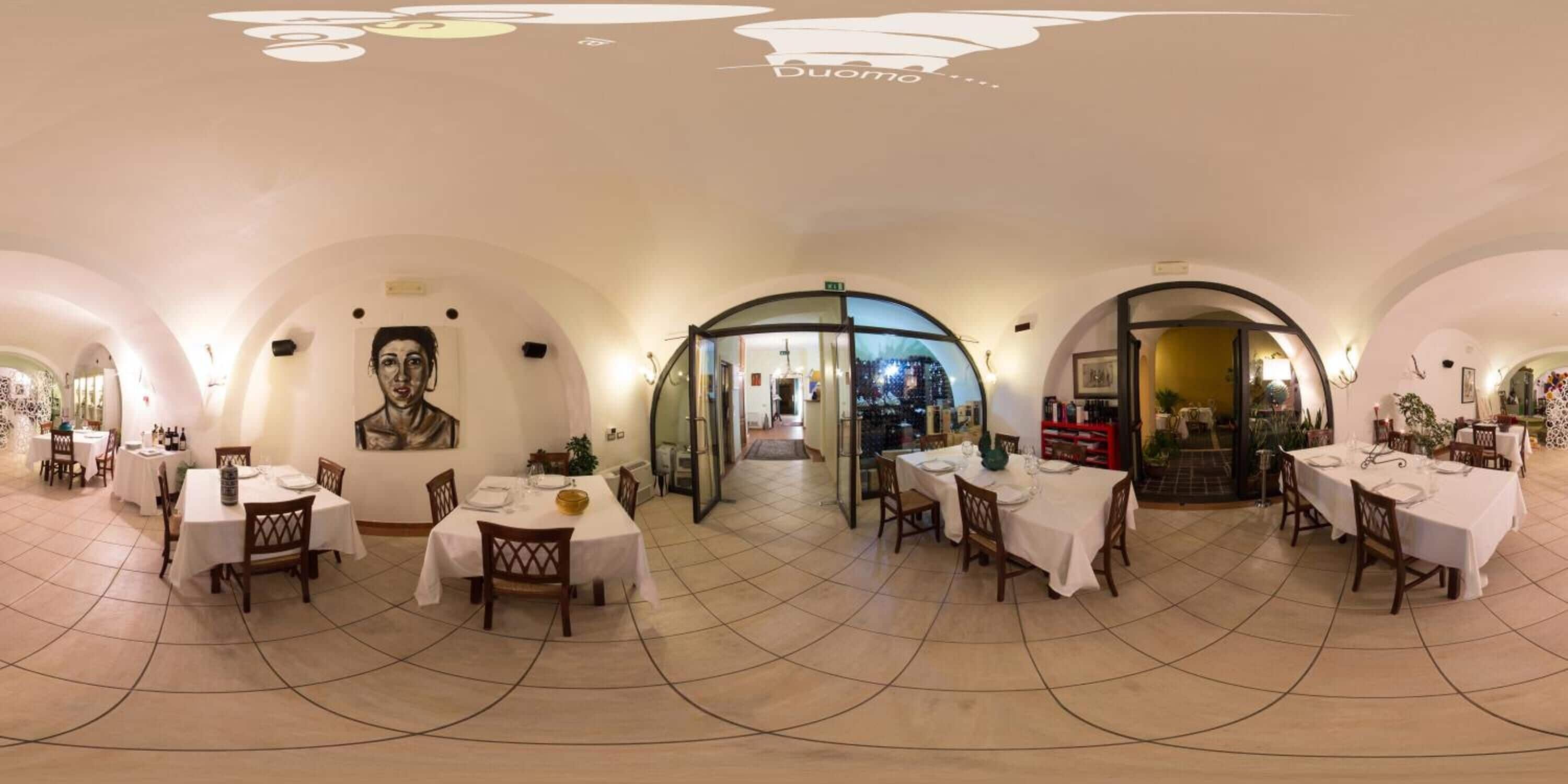 Un restaurante con varias áreas de comedor, cada una con mesas y sillas, y una entrada principal con puerta de vidrio.