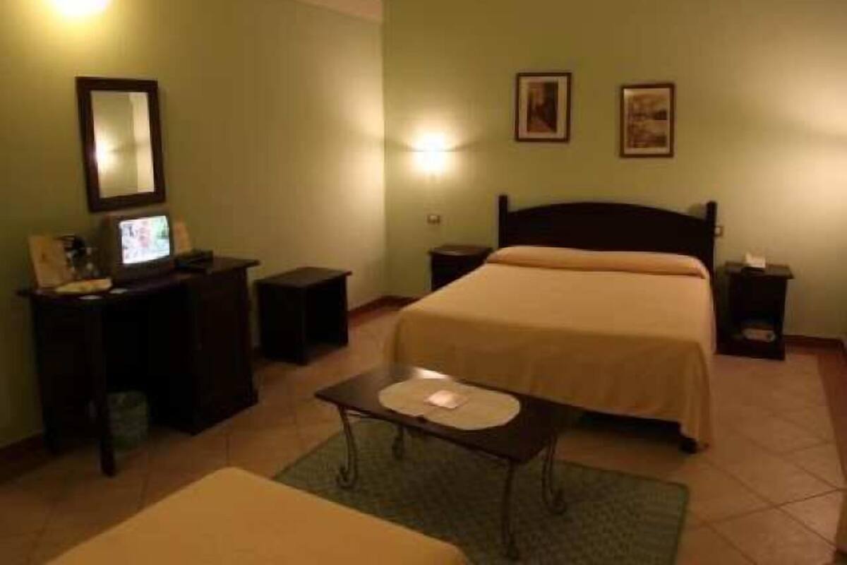 A hotel room with a bed, bedside tables, a desk with a computer, a chair, and a small table with a candle.