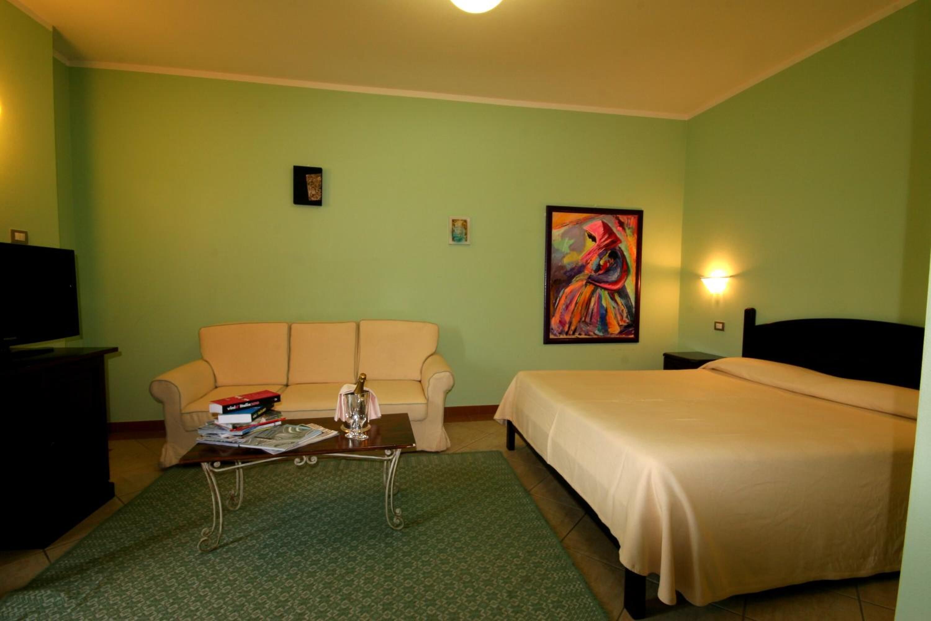 Habitación de hotel con cama, sofá, mesa de centro, televisor y un cuadro en la pared.