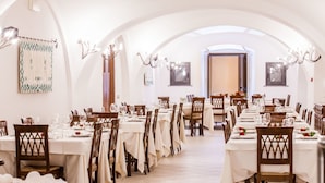 Un comedor amplio con mesas y sillas blancas, techos abovedados y candelabros.
