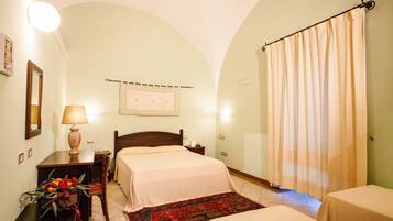 Una camera d'albergo con due letti, una scrivania con lampada, una sedia, un tappeto decorativo e una tenda.