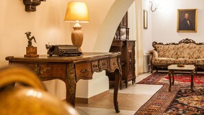Una habitación tradicional con un escritorio de madera, una lámpara, un sofá y una alfombra estampada.