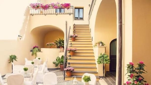 Un patio con una mesa lista para comer, rodeado de sillas y una escalera que lleva a un nivel superior.