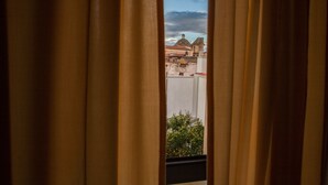 Vista a través de cortinas de un edificio con cúpula y tejado de tejas rojas.