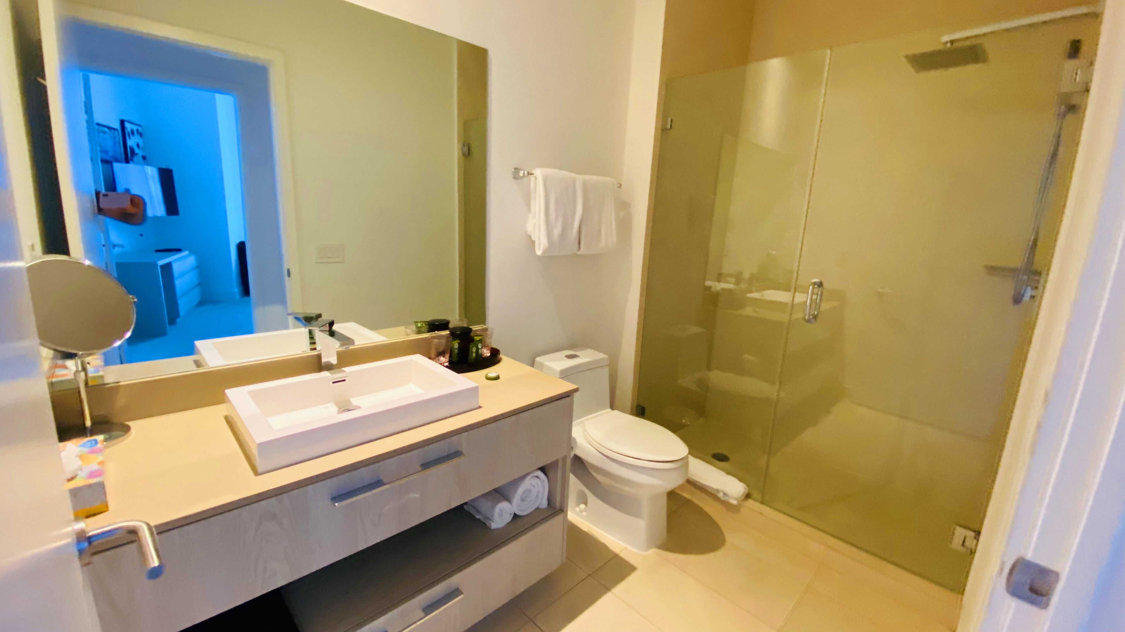 A modern bathroom with a large mirror, a sink, a toilet, and a glass-enclosed shower.