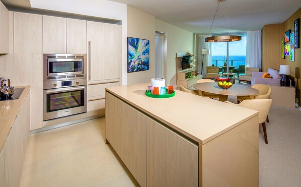 Een moderne keuken met een centraal eiland, geïntegreerde apparatuur en een eethoek met uitzicht op zee.