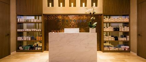 Un área de recepción de spa con un mostrador de mármol, estantes con productos de spa y una pared de mosaicos.