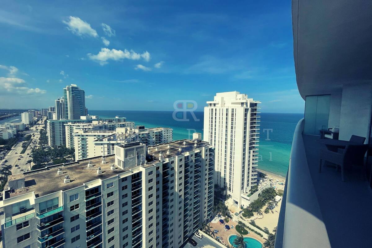 A high-rise building with a rooftop terrace, overlooking a beach and ocean.