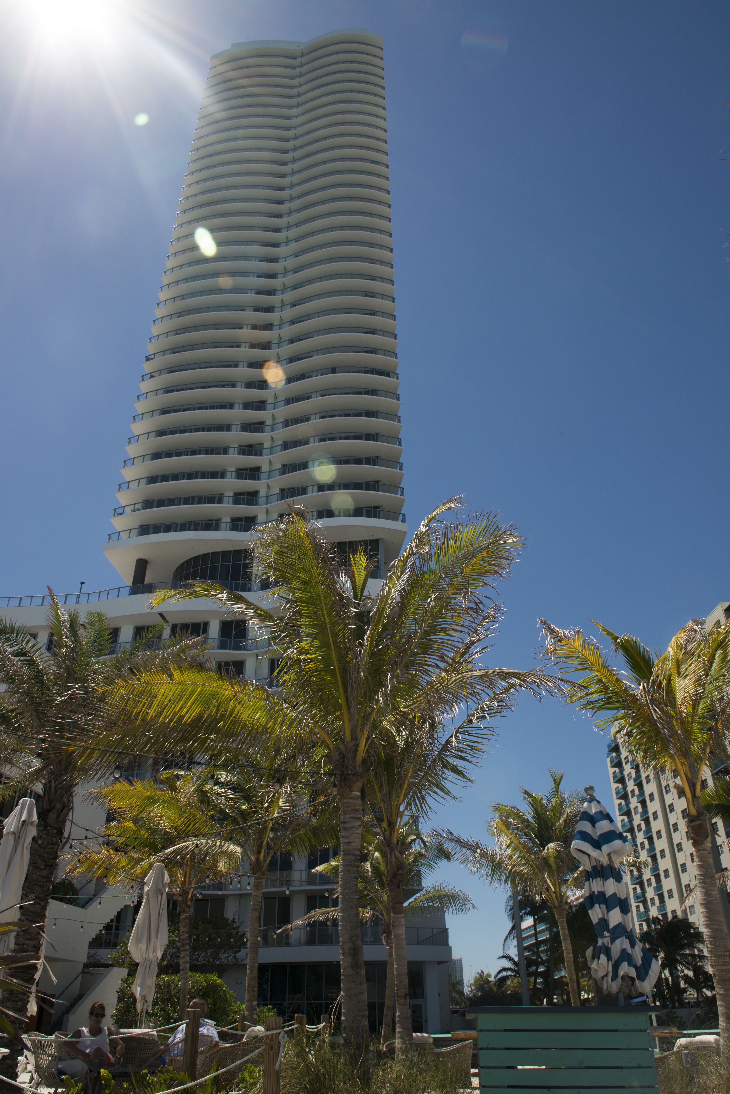 Un hotel alto y moderno con fachada curva, rodeado de palmeras y zonas de estar al aire libre.