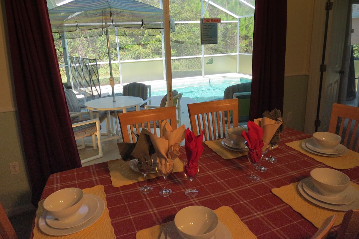 A dining table set for four with a red and white checkered tablecloth, white plates, and red napkins.