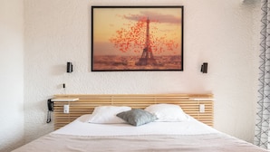Uma cama com roupa de cama branca, um travesseiro cinzento e uma cabeceira de madeira.