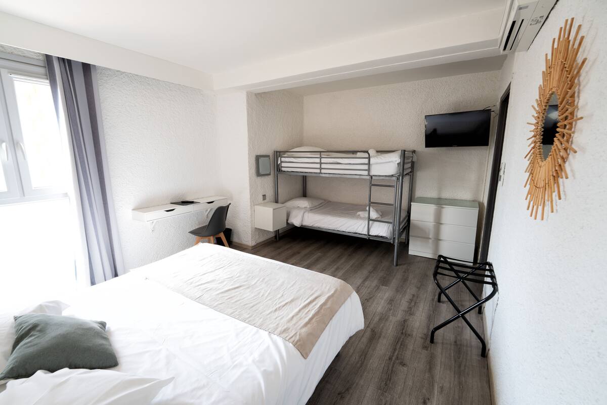 Une chambre d’hôtel avec un grand lit, un bureau avec une chaise, un lit superposé, un téléviseur à écran plat et un élément décoratif mural.