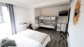 A hotel room with a large bed, a desk with a chair, a bunk bed, a flat-screen TV, and a decorative wall piece.