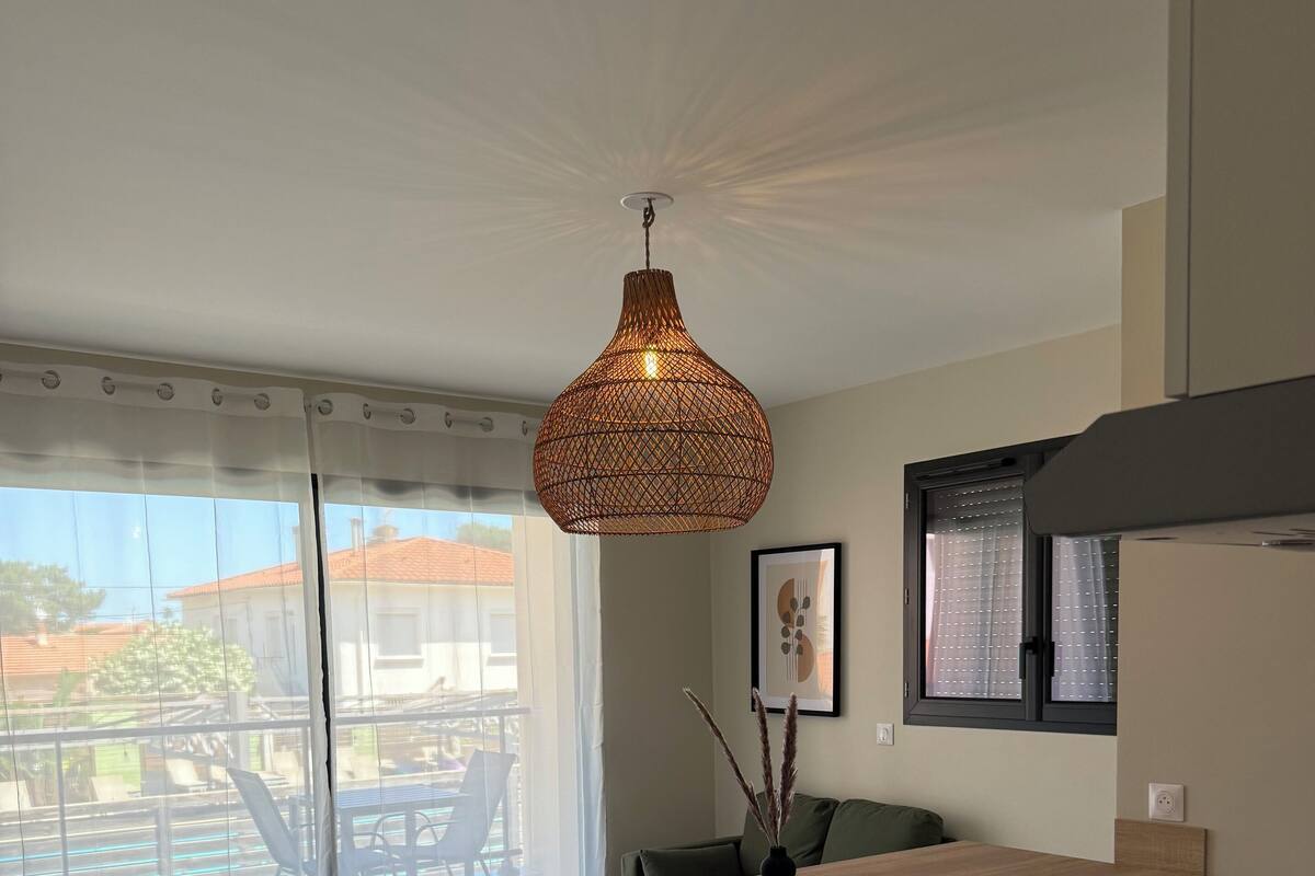 Une cuisine moderne avec un plan de travail en bois, des chaises blanches et un luminaire suspendu.